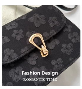 Close-up of black floral jacquard texture and elegant gold metal lock on crossbody bag