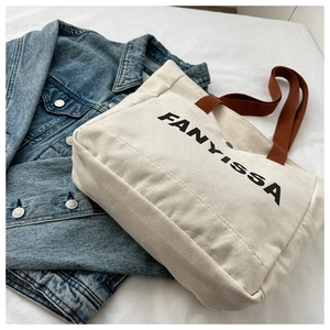 Detail of cream canvas tote bag with brown handles and black FANYISSA lettering