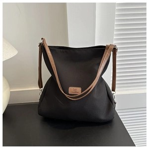 Detail view of large black canvas tote bag with brown straps and brand logo plate