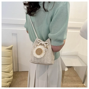 Detail of straw bucket bag with white daisy flower and drawstring strap on model