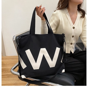 Détail du cabas en toile noire avec patch 'W' blanc et bandoulière réglable amovible