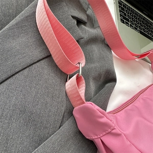 Pink canvas dumpling crossbody bag with wide shoulder strap on a grey suit jacket