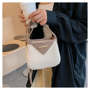 Detail of contrast stitching and V-shaped leather flap on a beige mini bucket bag