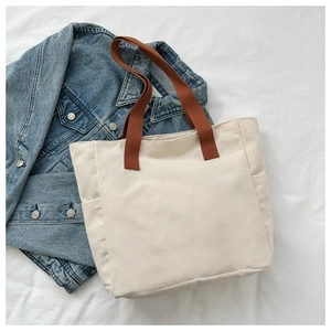 Detail of canvas tote bag showing side pocket, brown handles, and cream textile texture