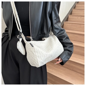 Detailed view of white pleated crossbody pillow bag with mini pouch on a black jacket