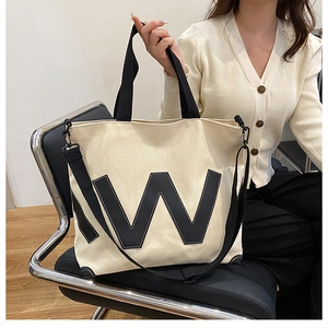 Détail d'un sac cabas en toile beige avec un patch lettre W noir et des sangles