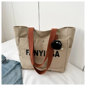 Close-up of canvas tote bag with orange strap, metal snap button and plush charm