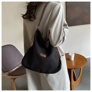 Detail of a large black canvas tote bag with adjustable brown leather straps and logo patch