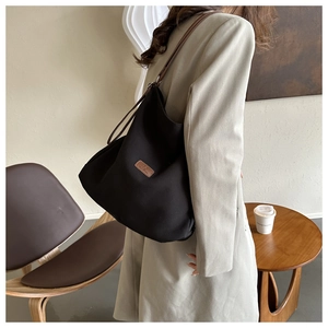 Detail view of a black tote bag with brown leather straps worn on shoulder by a model
