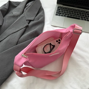 Pink canvas half-moon crossbody bag with items inside on a bed with a laptop