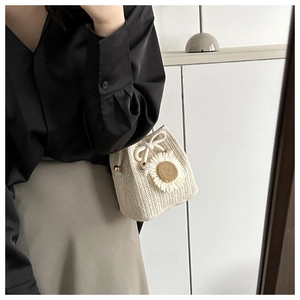 Detail of woven bucket bag featuring a large white daisy flower and drawstring closure