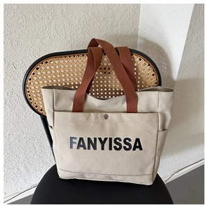 Detailed shot of large canvas tote bag with brown straps and FANYISSA text on black chair