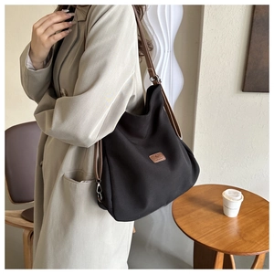 Detail of black canvas tote bag with brown leather straps and logo patch in minimal setting