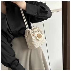 Detailed view of cream straw bucket bag featuring a 3D daisy flower and drawstring closure