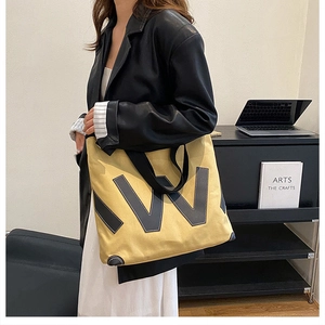 Détail du sac cabas en toile jaune avec écusson lettre W et coins renforcés en cuir