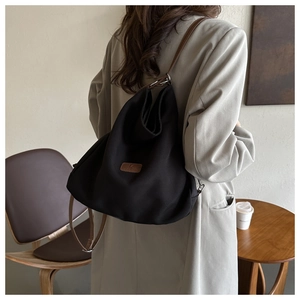 Detail of minimalist black canvas tote bag with brown straps and brand leather patch