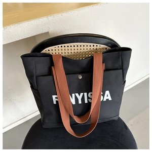 Close-up of FONYISSA black canvas tote bag with brown handles and a metal snap pocket