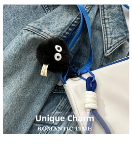 Close-up of a cute black fluffy soot sprite charm attached to a blue and white handbag