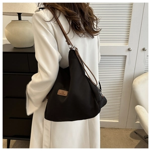 Detail of a black large canvas shoulder bag with brown leather strap and silver metal buckles