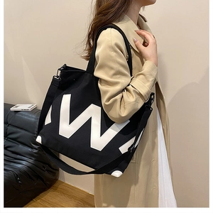 Détail du grand sac cabas noir en toile avec logo W blanc porté par un mannequin