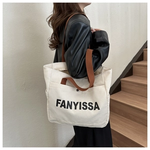 Detail of cream canvas tote bag with brown straps and side pocket held by a model