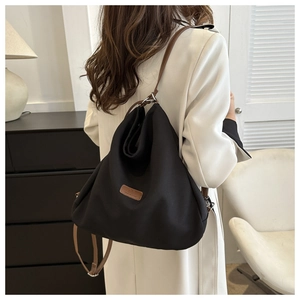 Detail of black fabric backpack with brown leather strap on model in professional setting