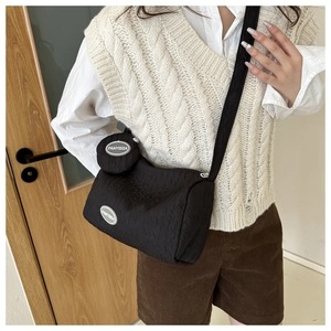 Detail shot of the black crossbody bag with a round coin pouch on a model's shoulder