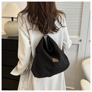 Detail of black canvas tote bag with brown leather logo patch on a model's shoulder