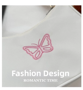 Détail de la broderie de papillon rose sur un sac à bandoulière blanc au design épuré