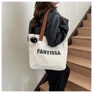 Detail of canvas tote bag with FANYISSA lettering and black plush monster charm