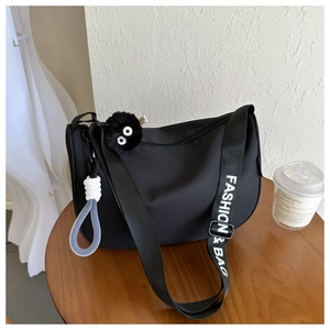 Close-up of black nylon crossbody bag featuring fashion-print strap and plush charm