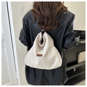 Detail of a cream canvas hobo bag with brown leather logo patch and silver hardware