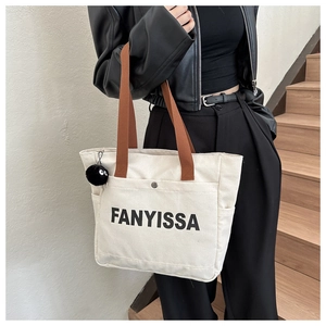 Detail of off-white canvas tote bag with black letters and brown straps worn by a model