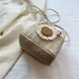 Beige straw bucket bag with a white daisy floral accent and cotton rope shoulder strap