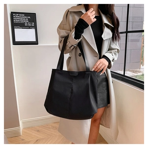 Gros plan d'un sac cabas en toile noire porté sur un trench-coat beige élégant
