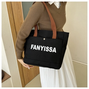 Detail of black canvas tote bag with white lettering and brown contrast shoulder strap