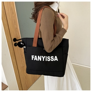 Close-up of black canvas tote bag with white lettering and orange shoulder strap