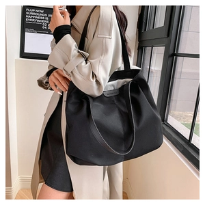 Close-up of a large black canvas tote bag with a minimalist leather logo on the front