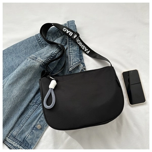 Detail of minimalist black crescent bag with branded wide strap and woven knot charm