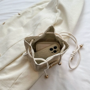 Minimalist straw woven bucket bag in cream white featuring golden drawstring accents
