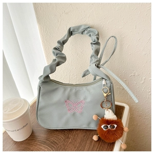 Détail du sac plissé vert clair avec broderie papillon rose et pendentif monstre en peluche
