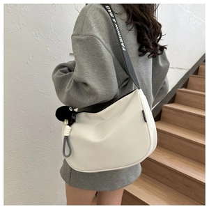 Detail of white crescent bag with gray strap featuring FASHION & BAG text and pompom