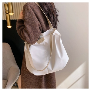 White oversized canvas tote bag with leather logo patch worn by a model in a minimalist setting