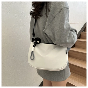 Minimalist white half-moon hobo bag with black nylon strap and fuzzy monster pendant