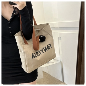 Detail of beige canvas tote bag with brown straps, side pocket and black pompom charm