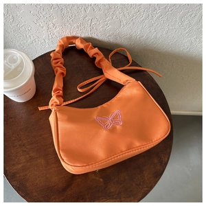Gros plan du sac sous le bras orange avec broderie papillon rose et bandoulière froncée