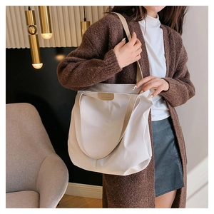 Large cream canvas tote bag with woven shoulder strap shown on a model in a modern interior