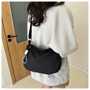 Detail of a minimalist black crossbody bag showing the fashion label and a rope knot pendant