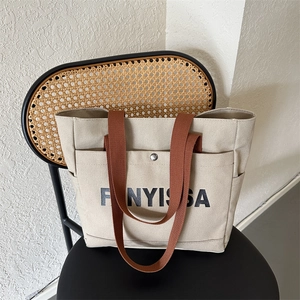 Minimalist beige canvas tote bag with brown straps and logo on a black chair