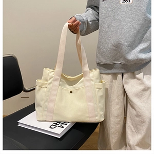 Close-up of cream canvas tote bag showing side storage pockets and metal snap button closure